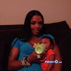 a woman sitting on a couch holding a baby and feeding it with a green bottle