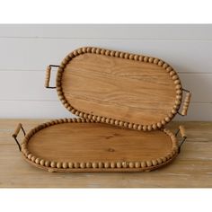 two oval wooden trays with beaded handles on top of a wood table next to a white wall