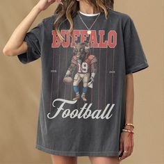 This retro Buffalo football t-shirt features a vintage illustration of a Buffalo holding a football dressed as a football player. This tee is the perfect gift for football fans or anybody who loves a good buffalo and football. This shirt is not associated with any team or league and is simply a piece of sports memorabilia for football fans in buffalo. This retro pinstripe football graphic t-shirt is an awesome piece of buffalo football merch for any sports fan or member of the mafia. This retro Football Season Fan Apparel T-shirt With Screen Print, Football Season Sports Fan T-shirt With Screen Print, Sports Fan T-shirt For Football Season With Screen Print, Football Season Sports Fan T-shirt, Football Season Sports Fan T-shirt For Streetwear, Football Season Sports Fan T-shirt With Sublimation Print, Retro Tops For Football Season Streetwear, Retro Tops For Streetwear During Football Season, Football Season Fan Merchandise Graphic Tee