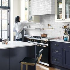 a woman standing in a kitchen next to a stove top oven and countertop with white tiles on it