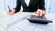 a woman in business attire sitting at a desk with a calculator and pen