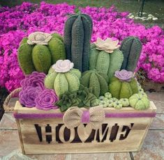 a wooden box filled with green and purple cactuses in front of pink flowered bushes