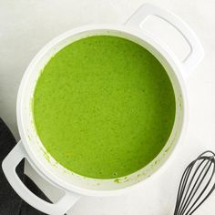 a white bowl filled with green liquid next to a whisk