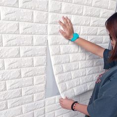 a woman standing in front of a white brick wall with her hands on the edge