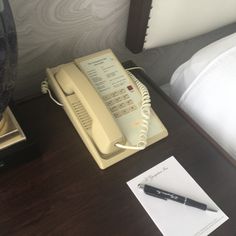 an old style telephone sitting on top of a desk next to a pen and paper