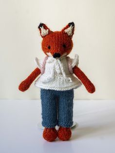 a knitted fox doll with blue pants and white shirt, standing on a table