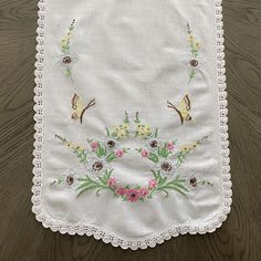 a white table cloth with flowers and butterflies on it sitting on top of a wooden floor