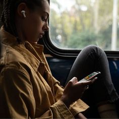 a woman sitting on a bus looking at her cell phone while listening to ear buds