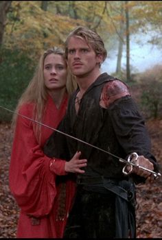 a man and woman dressed in medieval clothing standing next to each other on a forest path