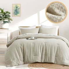 a bed with white sheets and pillows in a room next to a potted plant