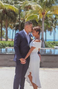 a man and woman standing next to each other in front of palm trees on the beach