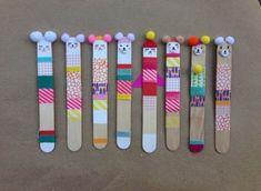 five wooden spoons decorated with animal faces and pom - poms, lined up in a row