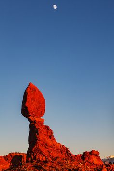 the moon shines brightly in the sky above balanced rock formations, with mountains and rocks below