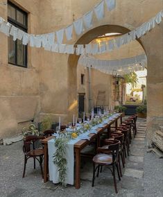 a long table set up with white linens and place settings for an outdoor dinner