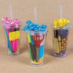 four plastic cups with different colored straws and pens in them on a brown surface