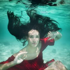 a woman in a red dress is under the water with her hair flying through the air