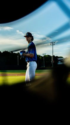 a baseball player walking across a field with his glove in his hand and the sky behind him