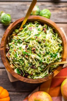 an apple and brussels sprout salad in a wooden bowl with two oranges on the side