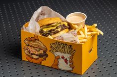 a hamburger and french fries in a yellow box on a black table with holes around the edges