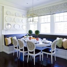 a dining room table with white chairs and plates on the wall above it, next to a window