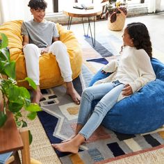 two people sitting on bean bag chairs in a living room with potted plants and large windows