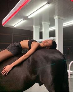 a woman laying on the back of a horse at a gas station with her eyes closed