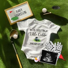 a baby's bodysuit and golf accessories are laid out on the green grass