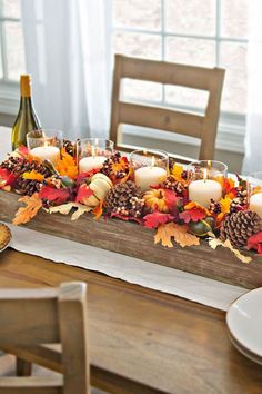 a wooden table topped with lots of candles and fall leaves next to a bottle of wine