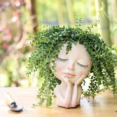 a doll with eyes closed sitting on top of a wooden table next to a plant