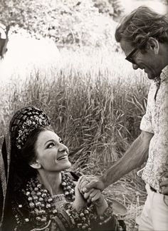 a man holding the hand of a woman who is sitting down in a field with tall grass