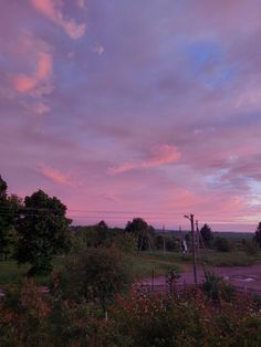 the sky is pink and purple as it sits over a field with trees in the foreground