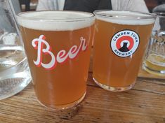 two beer glasses sitting on top of a wooden table