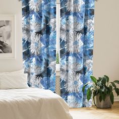 a white bed sitting next to a window covered in blue and white curtains on top of a wooden floor