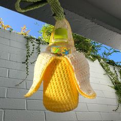 a crocheted banana hanging from a clothes line with a bottle in the back