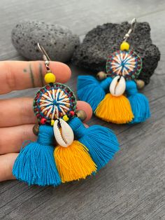 Unique fun and colorful earrings. Made with yellow and blue tassels and a beautiful round center piece made with different fabrics and strings, the earrings are adorned with beads, brass bells and shells. This pair will rock your outfit. Fun and easy to wear as they are super light. The earrings are 6cm- 2.40inch long 5.3cm- 2.10inch wide This timeless pair will brighten up your days! To see more unique and fun colorful tassel earrings, click the link below https://www.etsy.com/shop/AkashiJewelr Blue Tassel Drop Earrings For Festival, Beach Earrings With Latkans, Bohemian Beaded Tassel Earrings For Beach, Blue Festival Earrings With Latkans, Blue Fringe Earrings For Festivals, Bohemian Latkans Earrings For Beach, Blue Bohemian Earrings With Latkans, Bohemian Blue Earrings With Latkans, Bohemian Yellow Drop Earrings