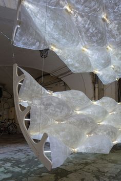 an artistic sculpture with lights hanging from it's sides in a room filled with white walls