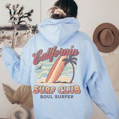 California Surf Club Hoodie, the perfect beachy sweatshirt for surf enthusiasts and coconut girls alike. This summer hoodie captures the essence of California's surf culture with its laid-back style and vibrant design. Made with high-quality materials, this surf hoodie is not only stylish but also comfortable, making it ideal for those breezy beach days or cozy nights by the bonfire. Channel your inner surfer with the California Surf Club Hoodie and embrace the carefree spirit of the California coast. 🖤 For oversized order 1-3 sizes up, refer to listing photos for sizes. RUNS ON THE SMALLER SIDE 🖤 Gildan 18500 🖤 Some Shrinkage may occur with washing 🖤 This unisex heavy blend hooded sweatshirt is relaxation itself.  🖤 Made with a thick blend of cotton and polyester, it feels plush, sof Blue Hooded Beach Tops, Blue Hooded Tops For Beach, Blue Hooded Top For Beach, Blue Hooded Tops For The Beach, Beach Season Long Sleeve Hoodie With Drawstring, Casual Surfing Hoodie With Graphic Print, Trendy Graphic Print Hoodie For Beach Season, Long Sleeve Hoodie With Letter Print For Surfing, Hooded Sweatshirt With Letter Print For Surfing