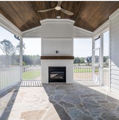 an empty covered porch with a fireplace and ceiling fan in the center, surrounded by white sidings