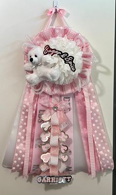 a teddy bear hanging from the side of a wall with pink ribbon and white polka dots