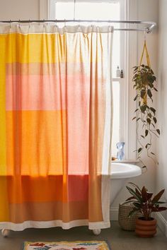 an orange and yellow striped shower curtain next to a bathtub with a potted plant