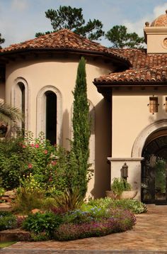 the front entrance to a house with flowers and plants around it, including an arched doorway