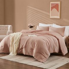 a bed with pink comforter and pillows in a room next to a white chair