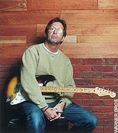 a man sitting in front of a brick wall holding a guitar