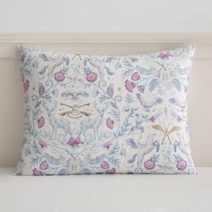 a white pillow with pink and blue flowers on it sitting next to a headboard