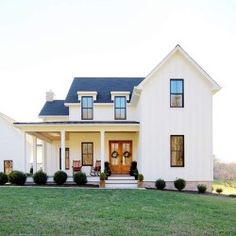 a large white house with black roof and two story windows on the front porch, surrounded by green grass