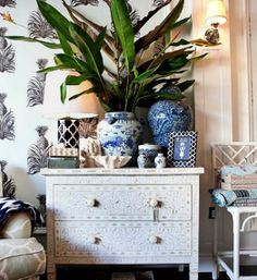 a white dresser with blue and white vases on it next to a palm tree