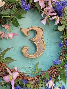 the letter 3 is surrounded by purple flowers and greenery on a blue background with gold metal letters