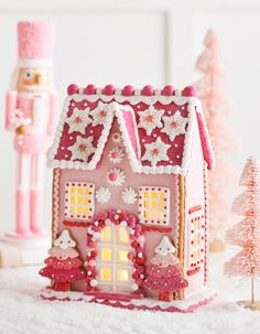 a pink gingerbread house next to a christmas tree and nutcracker on a table