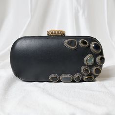 Hand-crafted with perfection, this luxury statement black leather clutch purse is exclusively embroidered with super-fine zardosi metallic thread. It's rarest combination of high-quality leather and zardosi metallic thread and genuine Onyx & Labradorite gemstones makes it opulent in its class. This comes under limited winter collection under the brand Zardouzee by Alark Lal. The metallic frame wrapped with leather looks awesome in parties and can also be carried easily in other formal events. With satin lining and pockets which can carry enough essentials like, mobile, small mirror, lipstick etc. Expertly hand embroidered by the most skilled zardozi artisans! Hand made in India! Size: 20*10*6 Utility: Shoulder Bag, Hand Clutch Bag Material: Leather, Metal Zari Stones: Onyx & Labradorite Ba Luxury Embellished Clutch Evening Bag, Luxury Embellished Evening Clutch Bag, Designer Leather Clutch For Party, Black Leather Evening Bag For Events, Designer Embellished Clutch For Evening, Designer Leather Evening Bag For Party, Elegant Clutch Evening Bag, Hand Embellished Black Evening Bag For Parties, Black Hand Embellished Evening Bag For Party