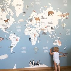 a baby standing in front of a wall with animals on it and the map of the world painted on it